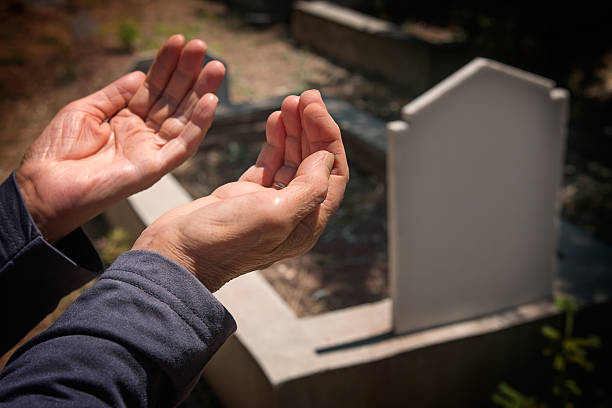 Hands raised in prayer beside a gravesite